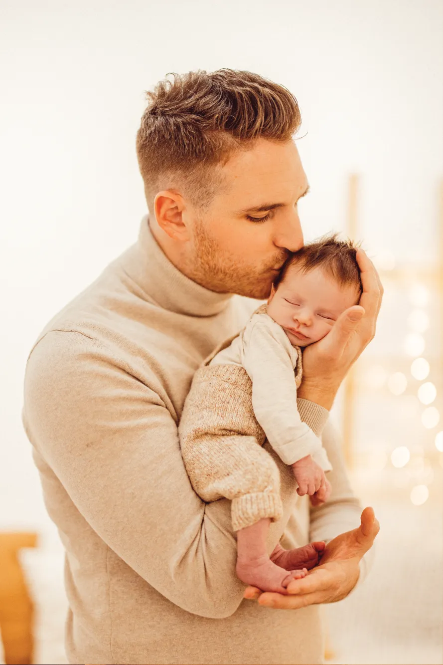 Vater und Baby in heller Kleidung liegen auf dem rechten Arm