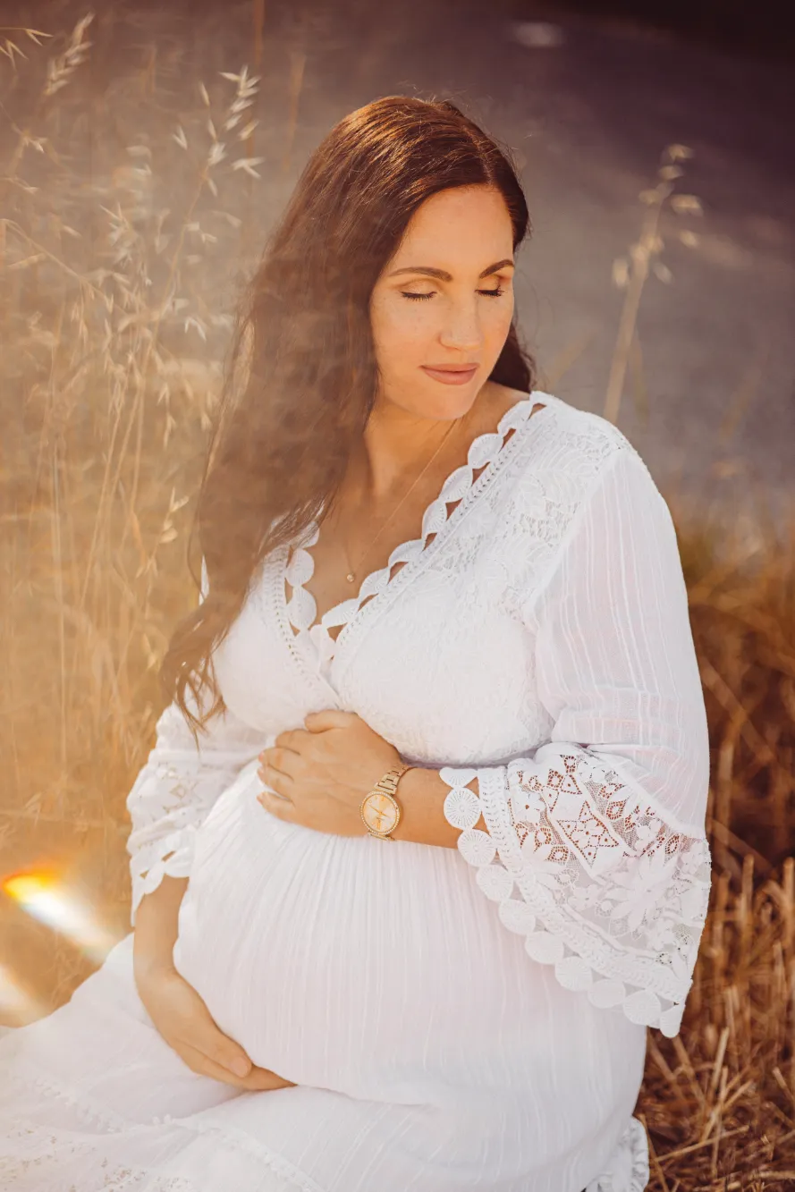 Schwangere Frau in weißen Kleid hält Ihre Hände auf ihren Babybauch