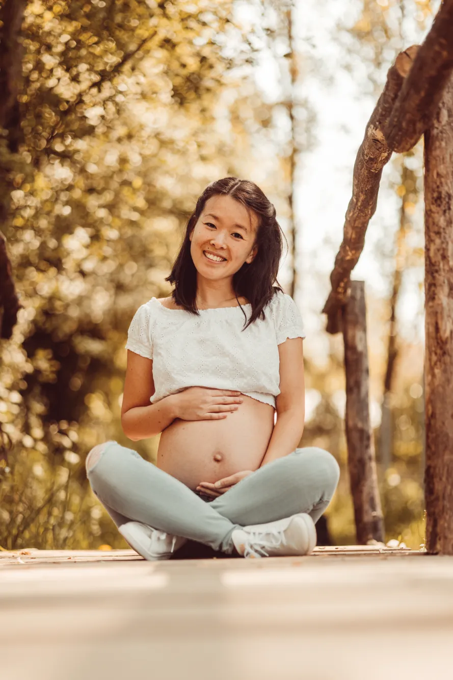 Eine lächelnde werdende Mutter, die ihr T-Shirt hochgezogen hat und ihren Babybauch mit beiden Händen hält.